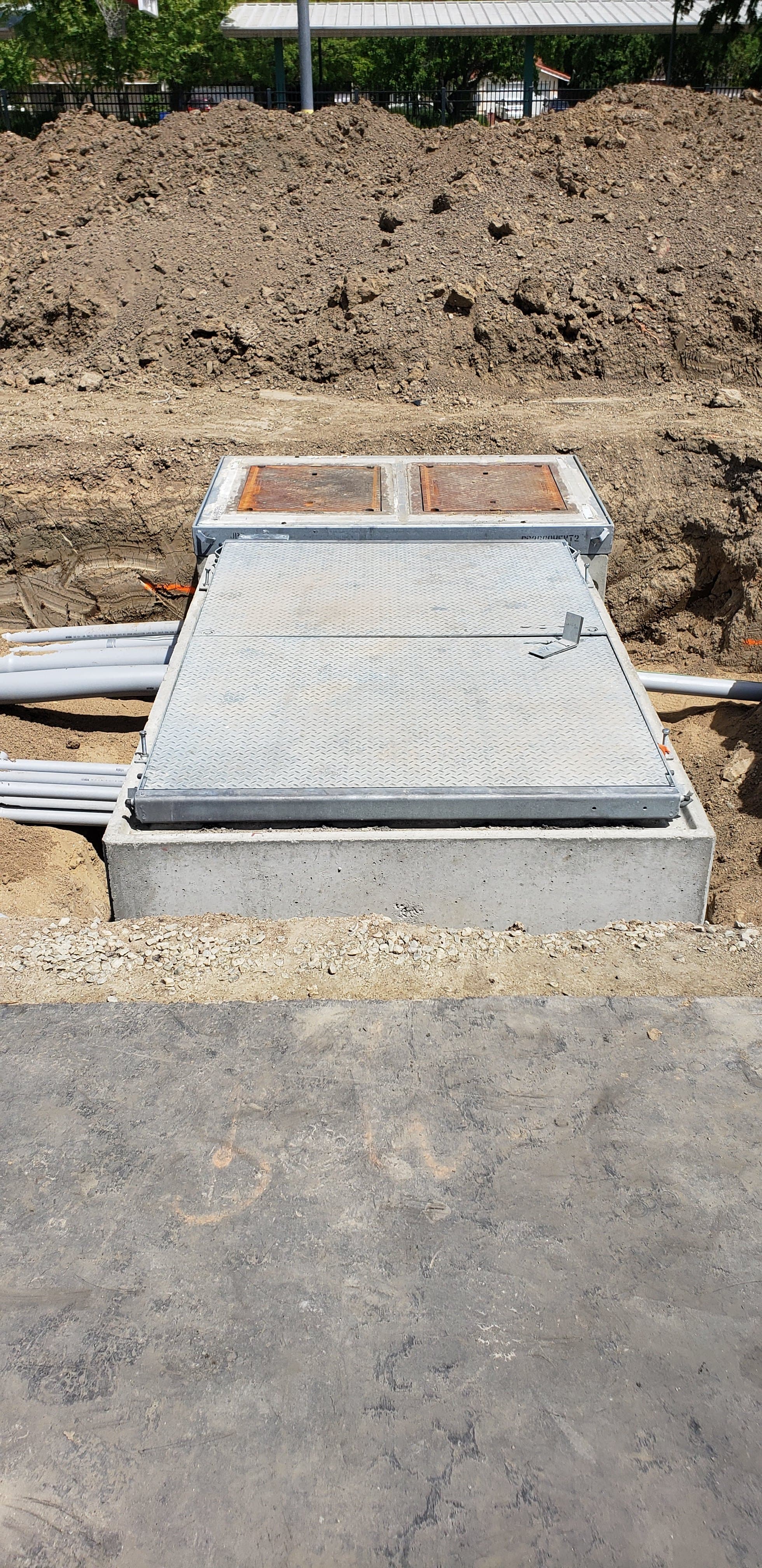 Racked PVC duct bank sweeping into a concrete underground pull vault at a commercial site
